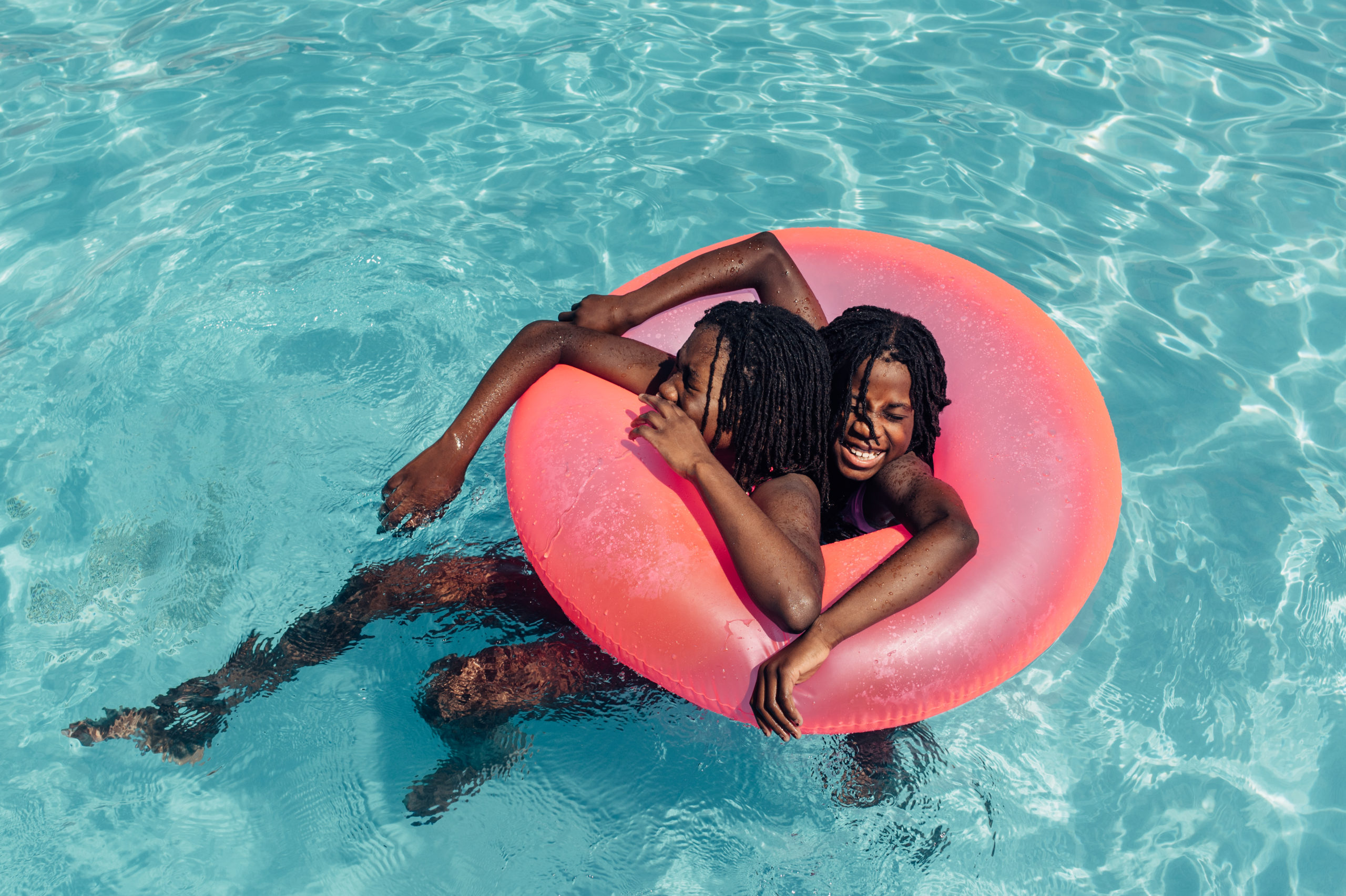 Two Black Girls In A Pool With A Pink Inner Tube