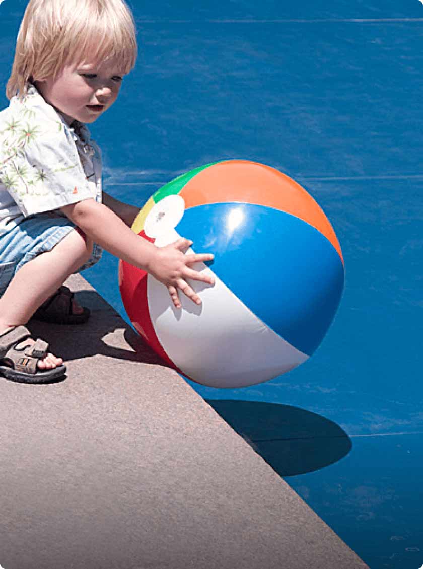 child on edge of pool with beach ball